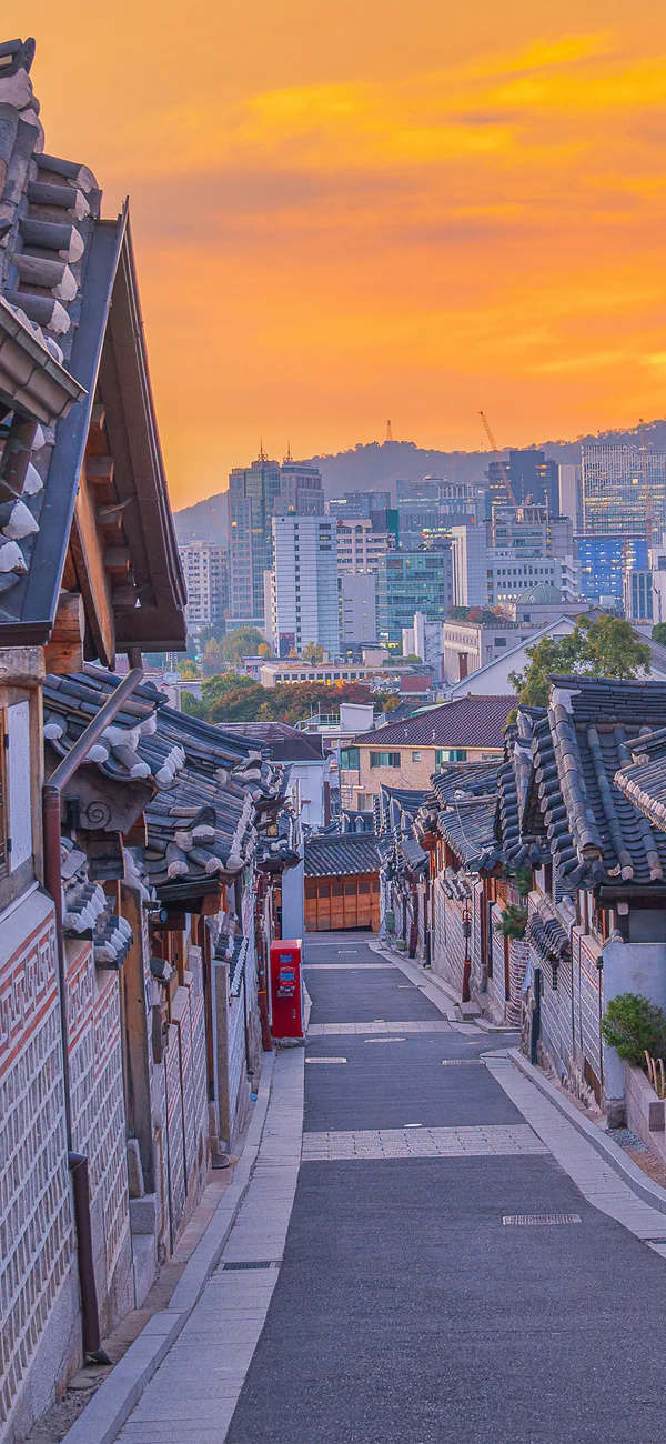 Solnedgang over Bukchon Hanok Village i Seoul, Sydkorea, med byens skyline i baggrunden