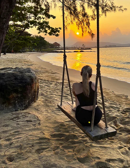 Person sidder på en gynge på en strand og nyder solnedgangen