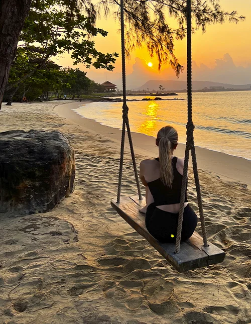 Person sidder på en gynge på en strand og nyder solnedgangen
