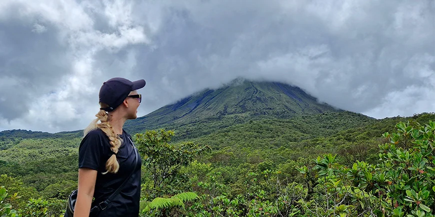 Nadia fra TourCompass foran Arenal-vulkanen på en skyet dag i Costa Rica