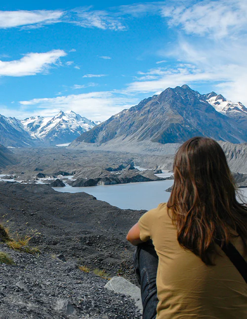 Person betragter de snedækkede bjerge og den smukke gletsjersø i Aoraki/Mount Cook Nationalpark, New Zealand