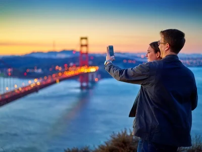 Mand og kvinde tager billede af Golden Gate Bridge ved solnedgang