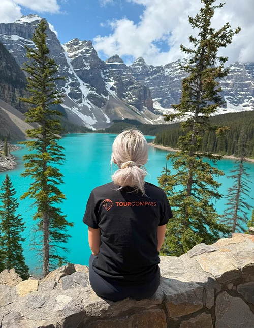 Kvinde med TourCompass t-shirt kigger ud over en turkisblå sø og sneklædte bjerge i Canada