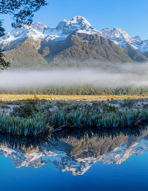 Mirror Lake, lavthængende tåge og sneklædte tinder på en klar vinterdag i Milford Sound, New Zealand