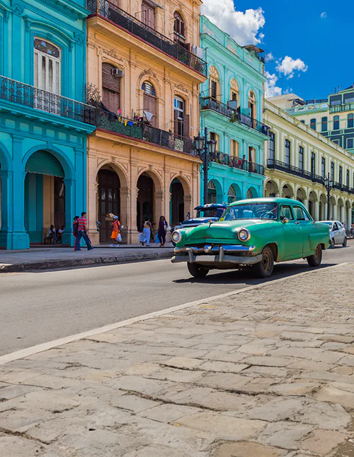 Farverige koloniale bygninger i Cuba og en klassisk grøn bil på en solrig bygade.