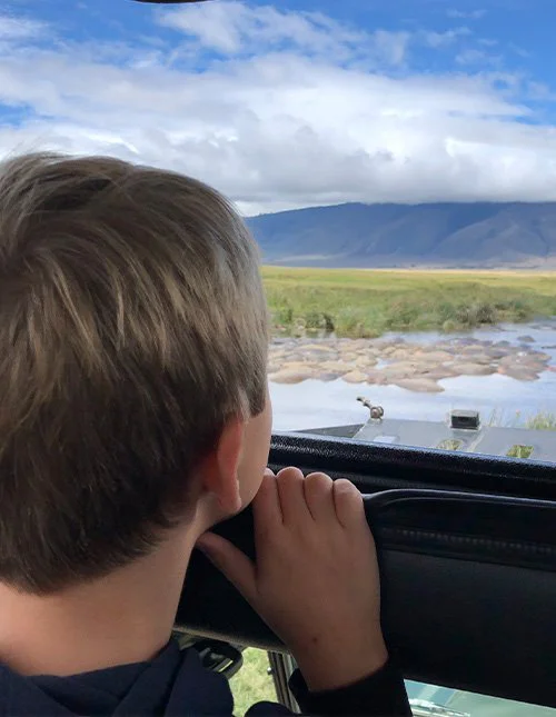 Et barn kigger ud fra en safaribil mod en flod og savannen