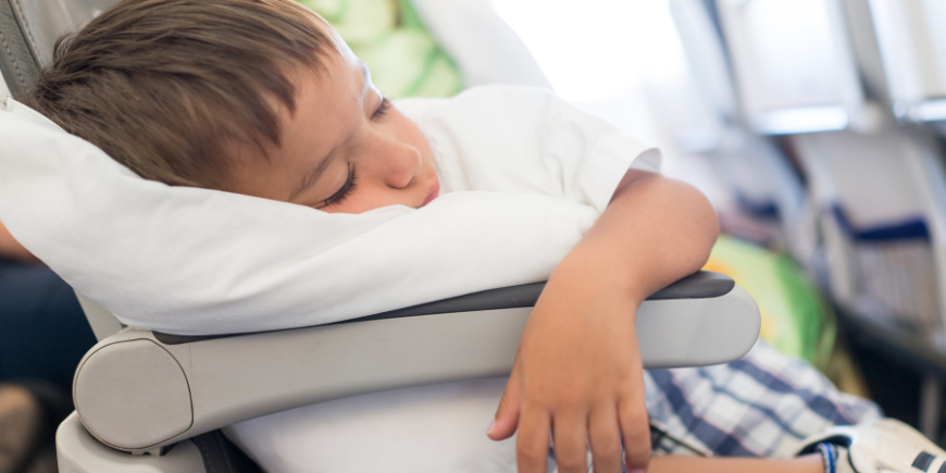 Dreng sover med pude i fly