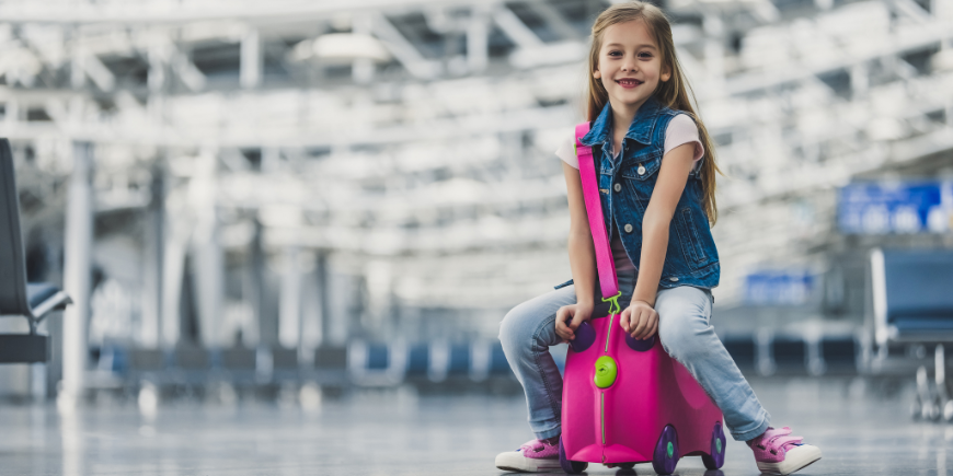 Barn sidder på en kuffert i en lufthavn