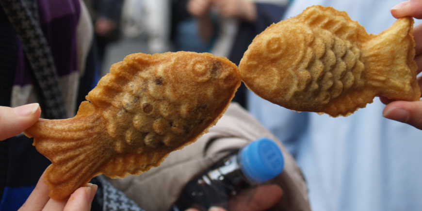 To personer holder taiyaki kager op, så det ligner fiskene kysser