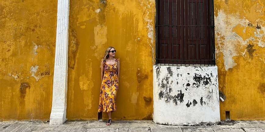 Kvinde i orange kjole, længer sig op ad orange væg i Izamal i Mexico.