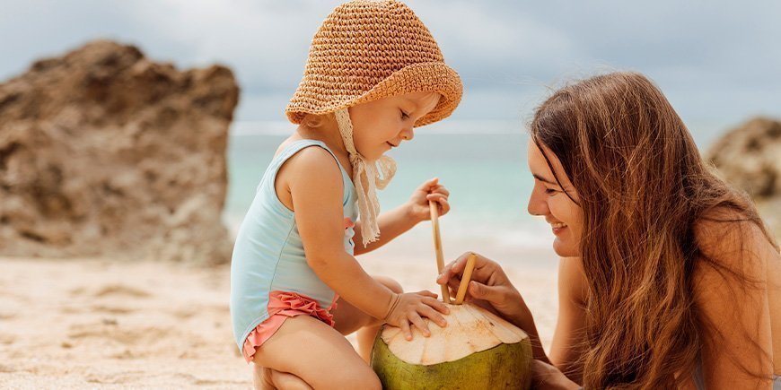 Mor og datter drikker fra kokosnød på strand i Thailand