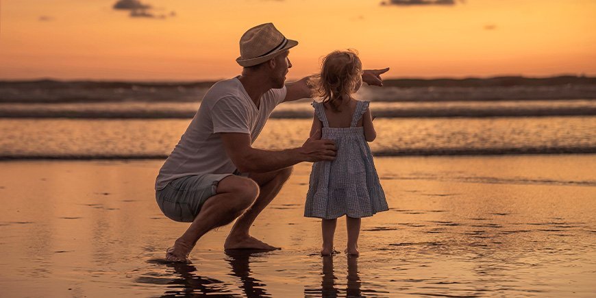Far og datter står på strand i Costa Rica ved solnedgang