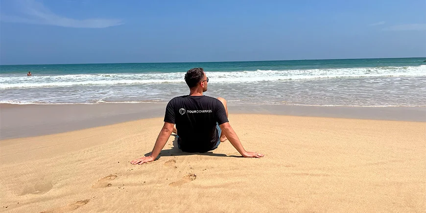 Mand i TourCompass t-shirt sidder på stranden i Mirissa i Sri Lanka