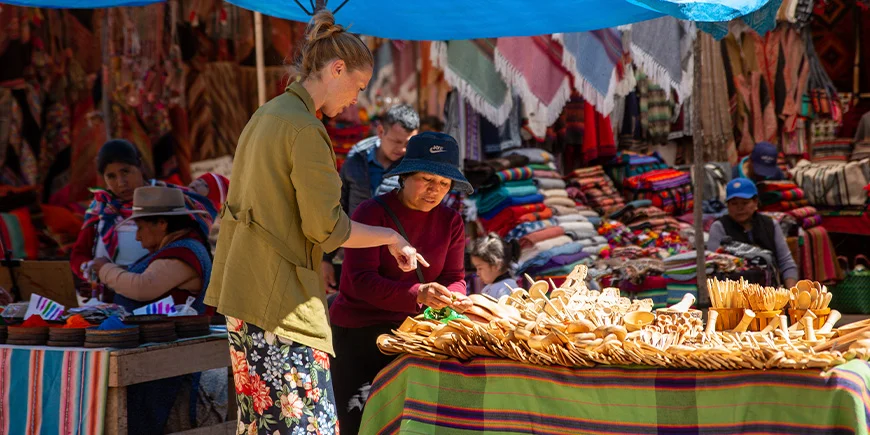 Kvinde taler med en lokal om de varer hun sælger på et marked i Cusco i Peru